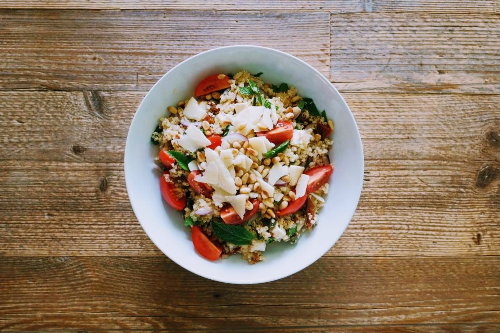 bunter, frischer Sommer-Quinoa-Salat mit leckeren Zutaten unkompliziert zubereitet, auf einem rustikalen Holztisch